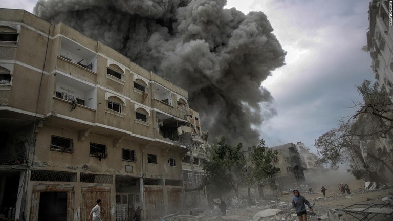 ガザ市中心部でのイスラエルの爆撃で、煙が立ち上る建物の周辺を走るパレスチナ人たち/AFP/Getty Images