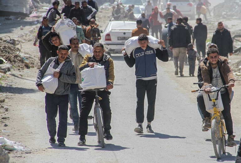 配布された支援物資を運ぶパレスチナの人々＝２３日、パレスチナ自治区ガザ地区ガザ市/Mahmoud Issa/Reuters