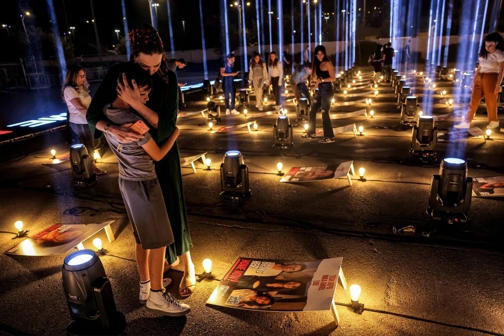 10月7日の攻撃でハマスに拉致された人質の写真の間に立ち、抱き合う女性と子ども/Ahmad Gharabli/AFP/Getty Images