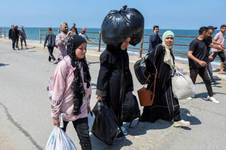 袋を頭にのせ、二つの荷物を両手に下げて移動するウム・モハマドさん（中央）＝１４日/Ramadan Abed/Reuters