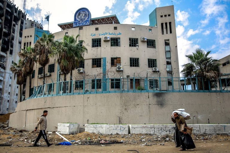 国連パレスチナ難民救済事業機関（ＵＮＲＷＡ）のガザ拠点の前を通り過ぎる人々/AFP/Getty Images