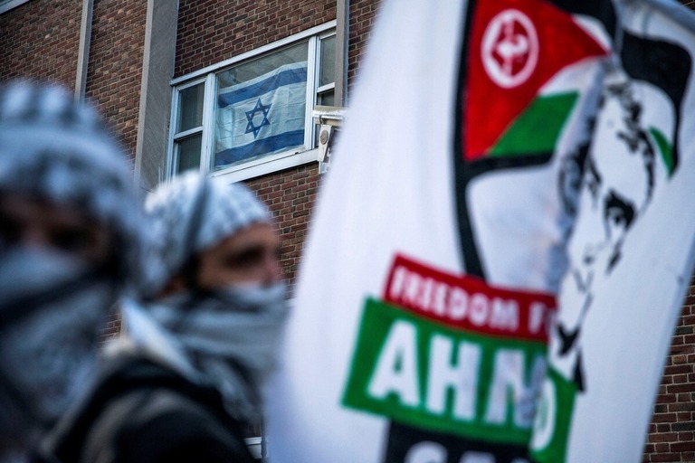 デモ参加者らと背後の建物の窓に掲げられたイスラエル国旗＝２３日、米ニューヨーク市のコロンビア大学周辺/Eduardo Munoz/Reuters