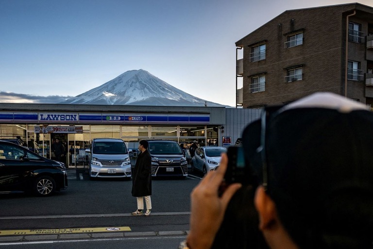 富士河口湖町のコンビニの前で遠景の富士山を撮影する観光客/Philip Fong/AFP/Getty Images via CNN Newsource