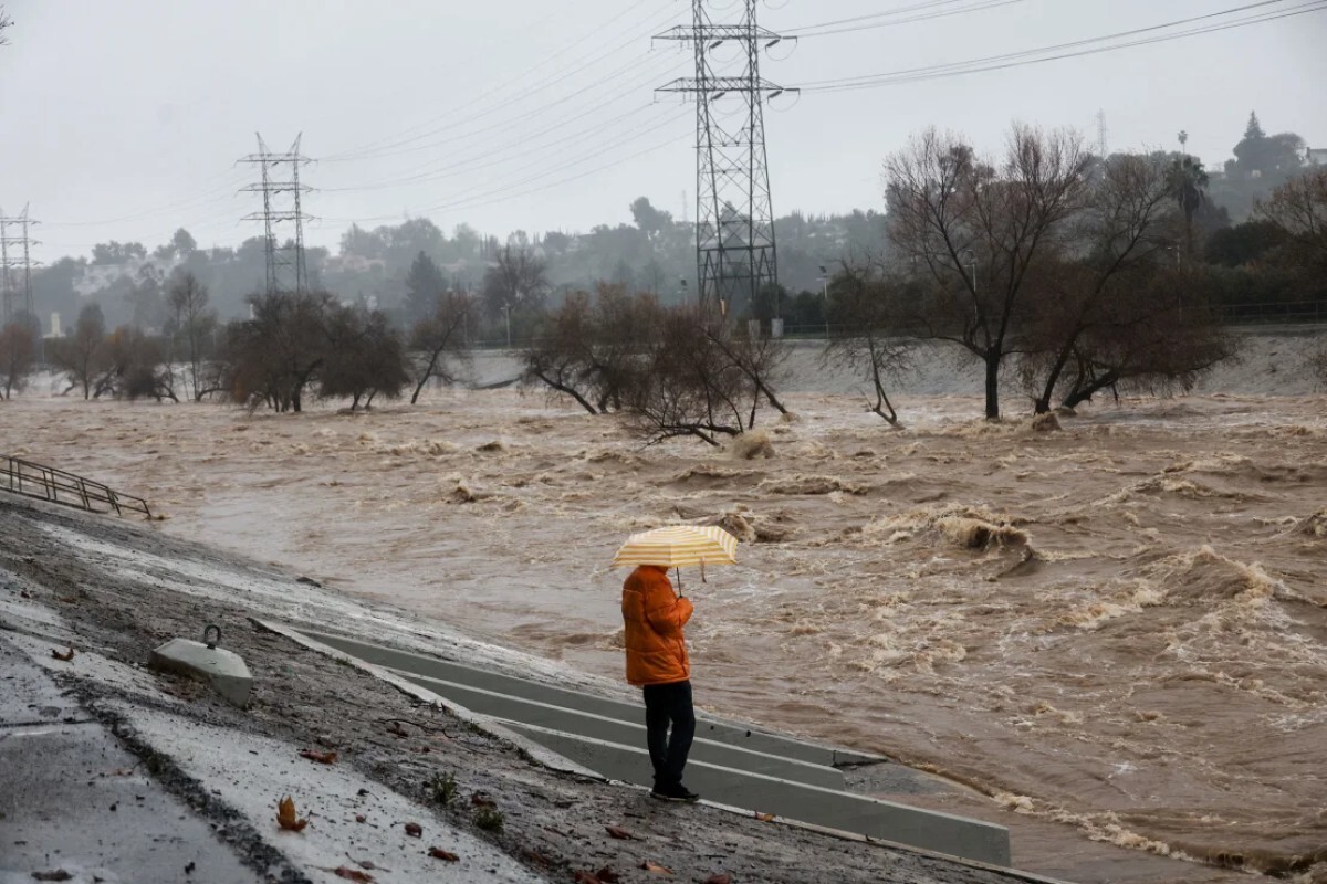 ロサンゼルスを襲った豪雨の中、傘を手にロサンゼルスの川を見つめる男性=24年2月5日/Aude Guerrucci/Reuters