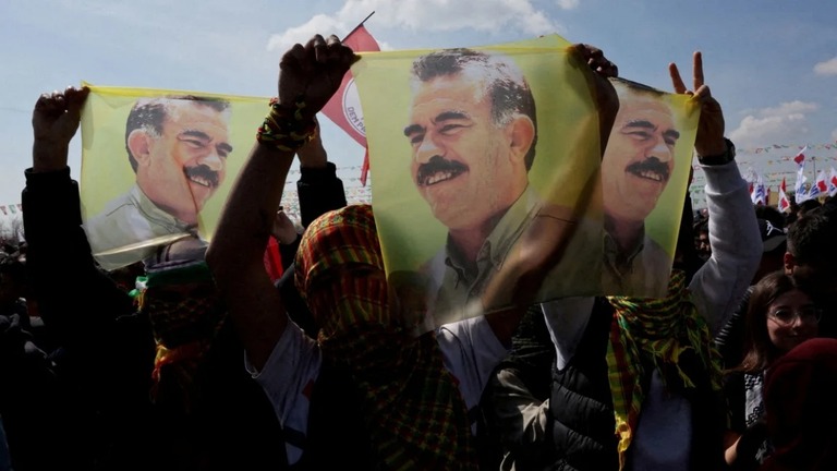 「クルディスタン労働者党（ＰＫＫ）」の指導者アブドラ・オジャラン氏が描かれた旗を掲げて集会に参加する人々＝２０２４年３月、トルコ・イスタンブール/Umit Bektas/Reuters/FILE