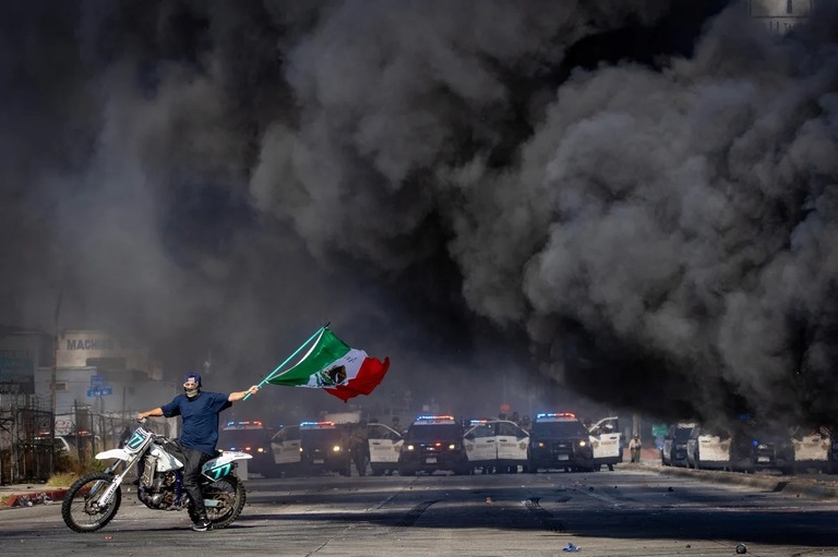 警官とデモ隊が衝突するなか、バイクにまたがりメキシコ国旗を振る男性＝７日、米カリフォルニア州パラマウント/Barbara Davidson/Reuters