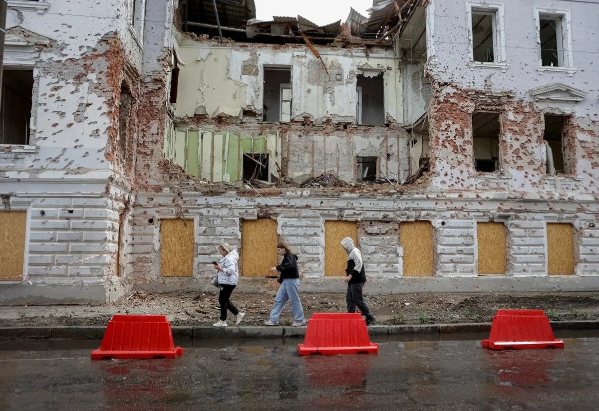 ロシア軍のミサイルによって破損した建物の前を歩く住民=13日、ウクライナ・スーミ州/Sofiia Gatilova/Reuters