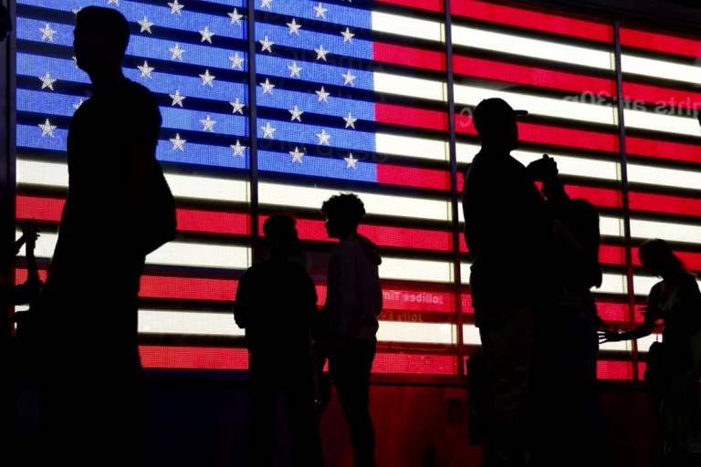 米ニューヨークのタイムズスクエアで、星条旗が写ったスクリーンの前に立つ人々/Ludovic Marin/AFP/Getty Images